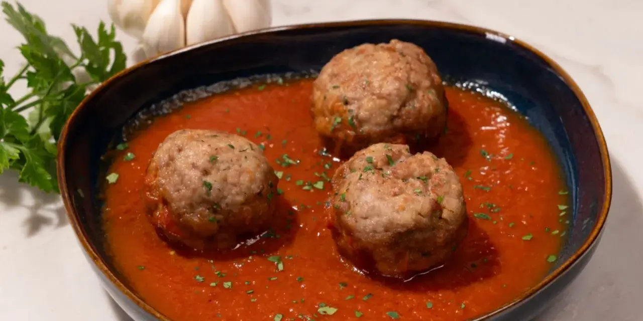 Tres albóndigas caseras en una rica salsa de tomate, adornadas con perejil fresco. Un plato reconfortante que evoca la cocina tradicional.