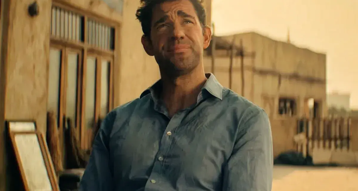 John Krasinski w niebieskiej koszuli, zamyślony. Widzimy fragmenty jego filmów, seriali i programów.