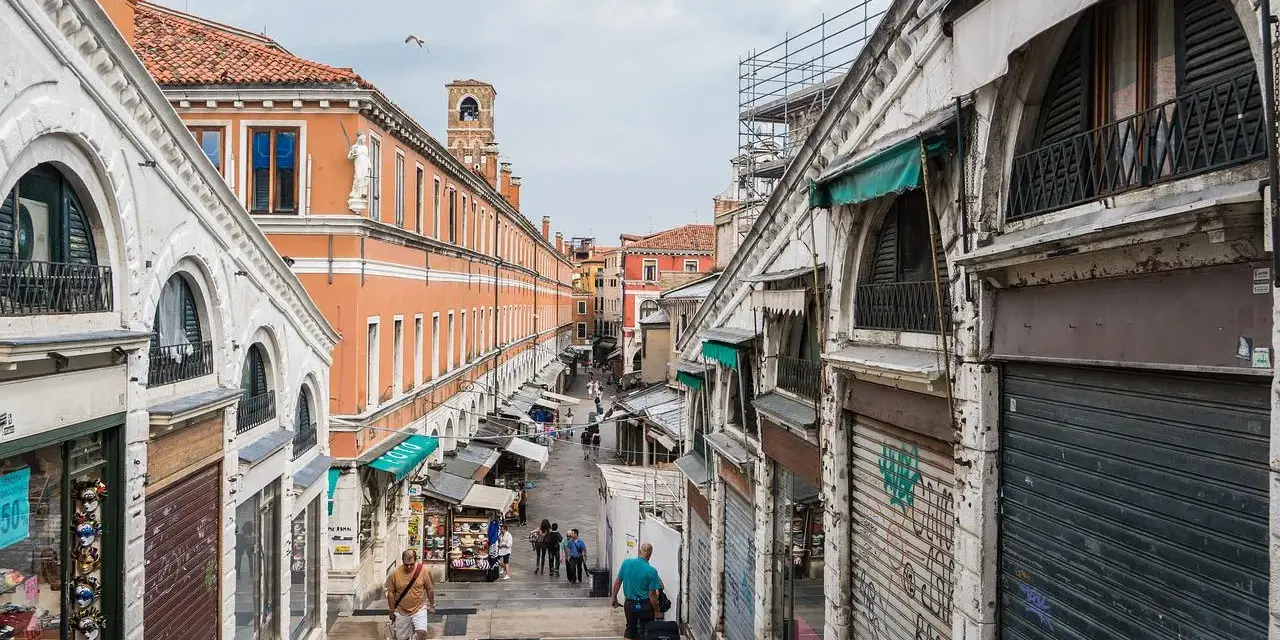 Scendendo le scale del ponte di Rialto a Venezia, si intravede un mercato vivace con negozi e bancarelle.