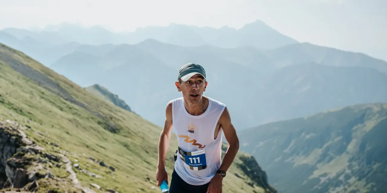 Zawodnik z numerem 111 biegnie pod górę podczas Tatra Sky Marathon. W tle piękne, mgliste pasmo górskie.