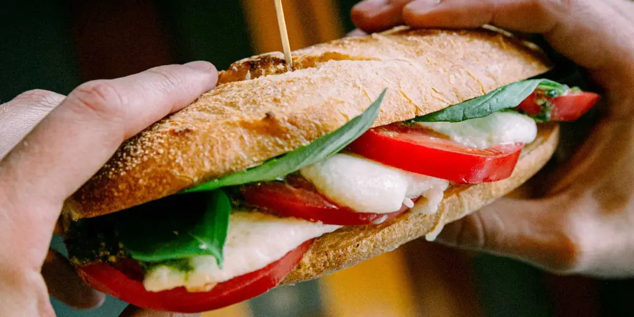 Ręce trzymają pyszne włoskie pieczywo z mozzarellą, pomidorami i bazylią. Idealne na szybki lunch.