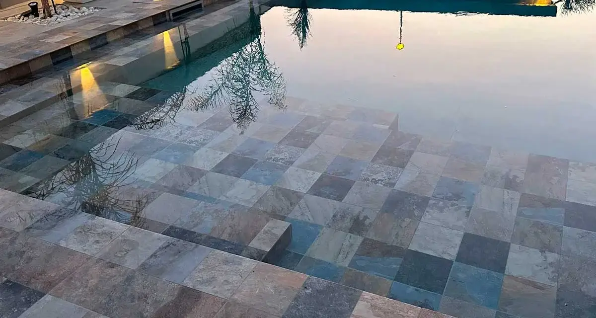 Escalones de piscina con diversos tipos de gresite para piscinas, creando un mosaico de tonos grises, azules y marrones.