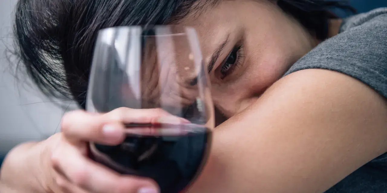 Smutna kobieta z kieliszkiem wina, jakby słuchała piosenki o alkoholu.