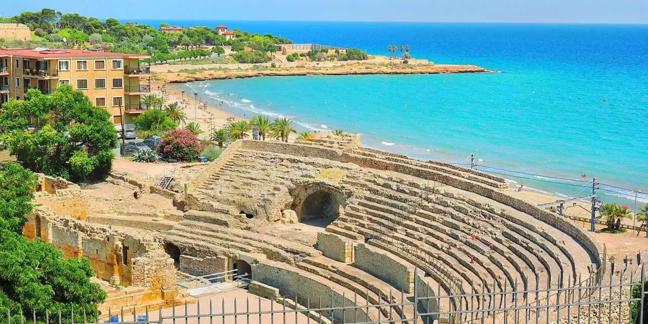 Ancient Roman amphitheater ruins overlooking a beautiful beach and turquoise sea. Discover Tarragona things to do, from history to relaxation.