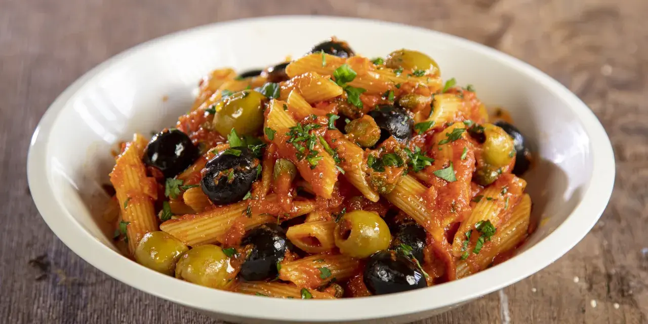 Penne con sugo rosso, olive nere e verdi, capperi e prezzemolo. Un piatto di pasta alla puttanesca invitante e saporito.