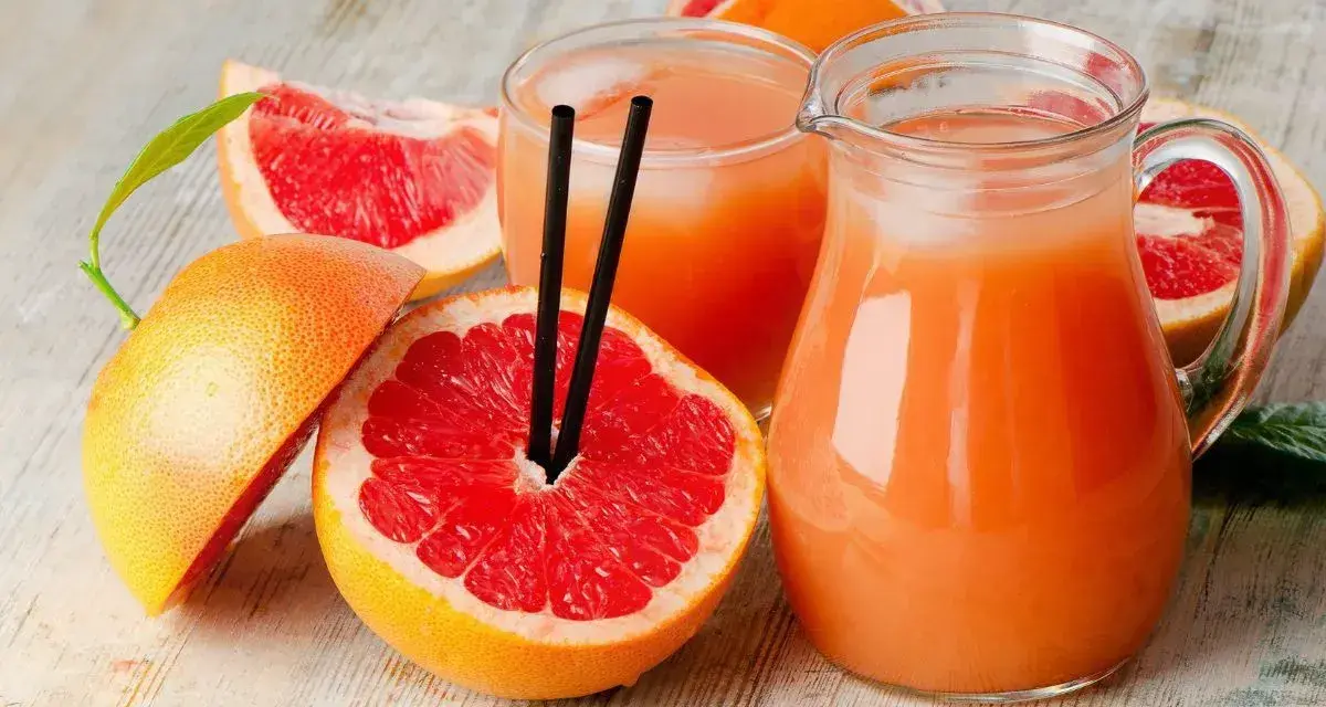 Orzeźwiający drink z grejpfrutem, podany w dzbanku i szklance, otoczony świeżymi owocami. Idealny na upalne dni.