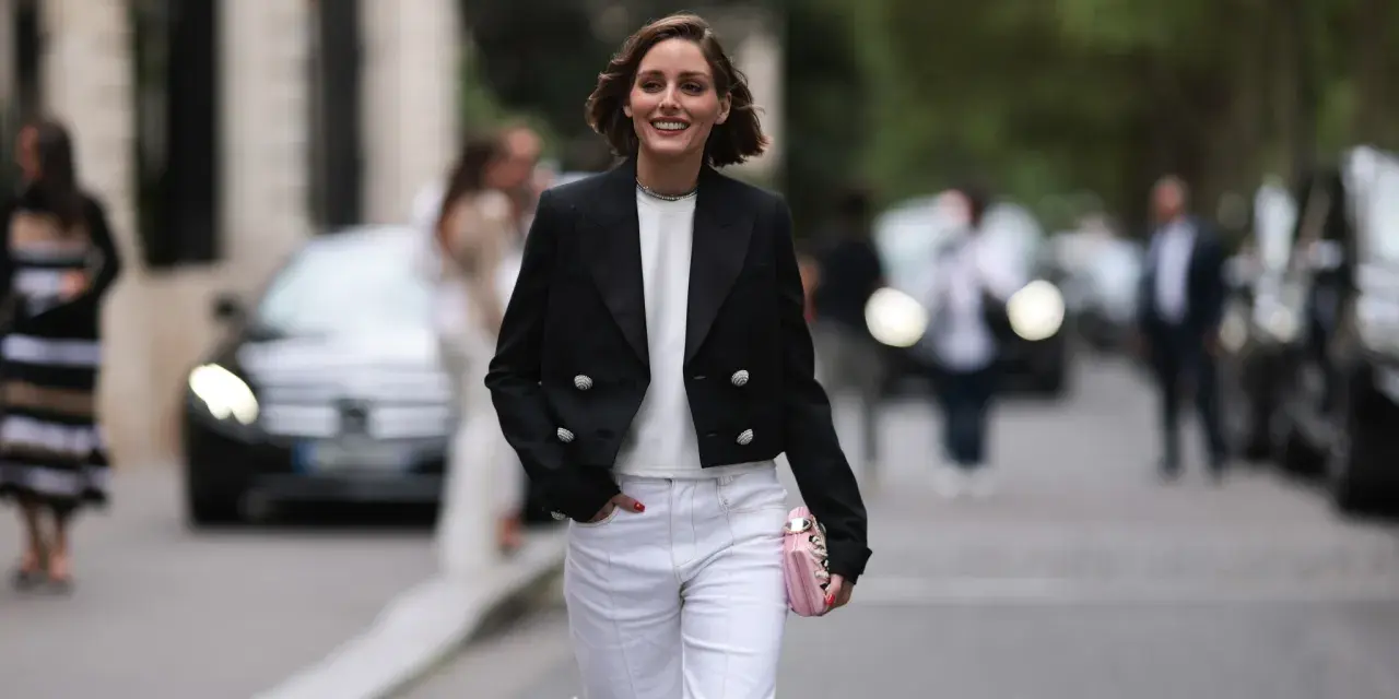 Mujer sonriente con chaqueta negra y pantalones blancos, lista para una comida familiar de invierno.