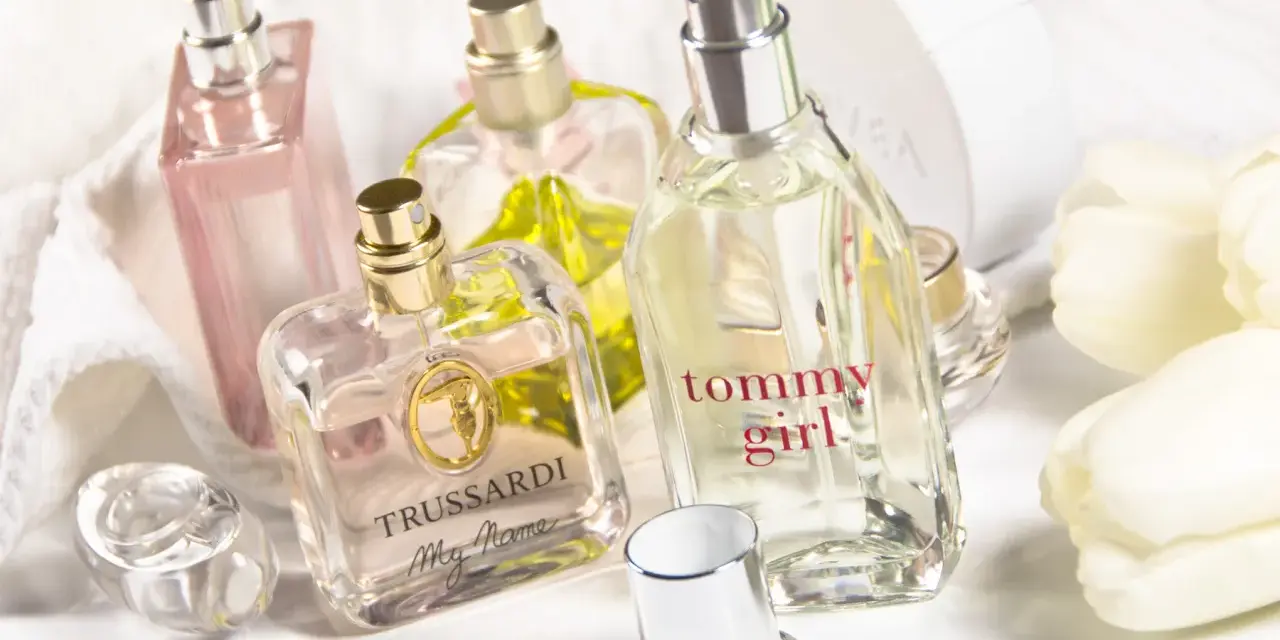 Mehrere Parfümflaschen, darunter Trussardi und Tommy Girl, auf weißem Handtuch mit weißen Tulpen.