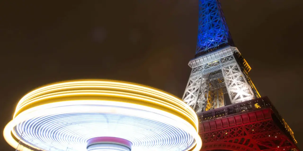 Manège lumineux tournant devant la Tour Eiffel illuminée en bleu, blanc et rouge. Une scène de Paris nocturne, parmi les plus belles photos de nuit.