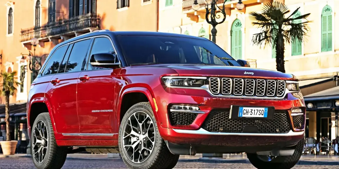 Czerwony Jeep Grand Cherokee zaparkowany na brukowanej ulicy przed budynkami z balkonami.