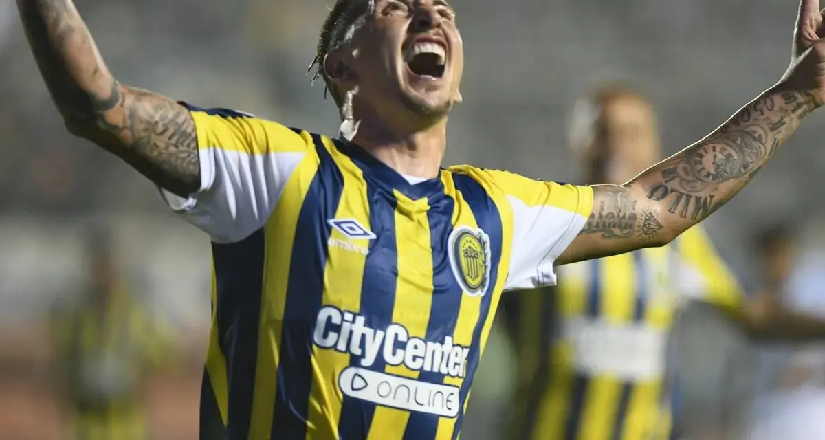 Jugador de Rosario Central celebra un gol, con los brazos en alto y la boca abierta. Sus tatuajes son visibles en sus brazos.