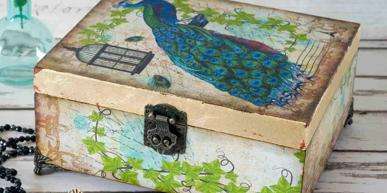 Ozdobna szkatułka z pawiem, klatką i liśćmi. To przykład techniki decoupage, która pozwala na piękne zdobienie przedmiotów.