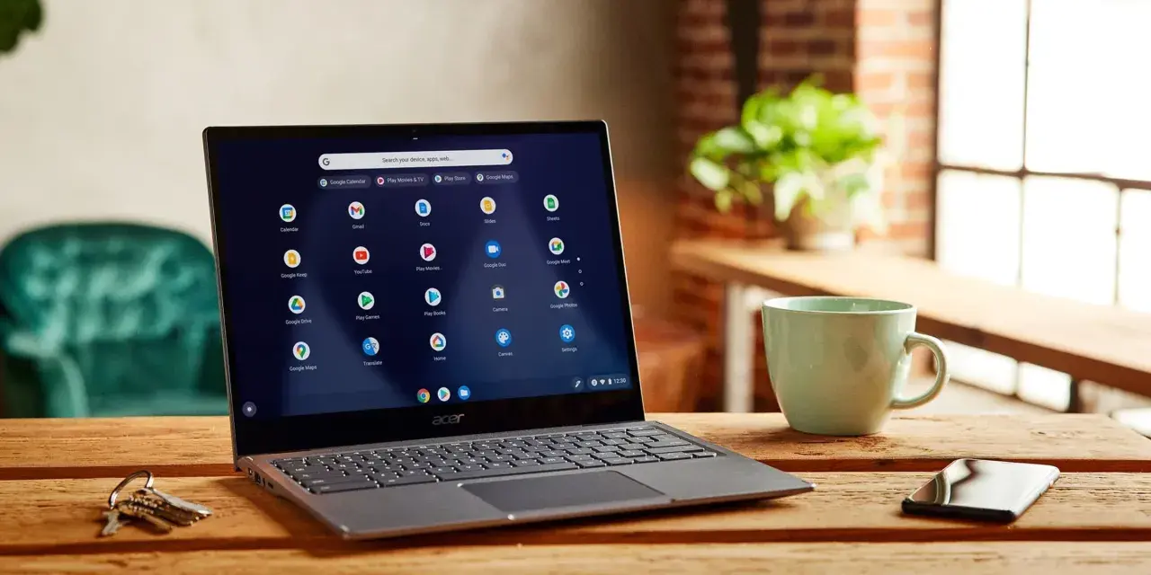 Laptop z systemem Chrome OS Flex na drewnianym stole, obok kubek i klucze.