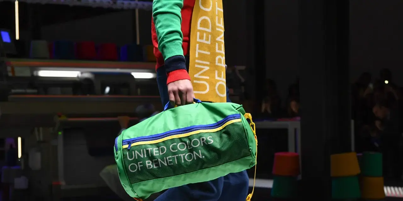 Zielony worek z napisem "UNITED COLORS OF BENETTON" niesiony przez modela w kolorowym swetrze.