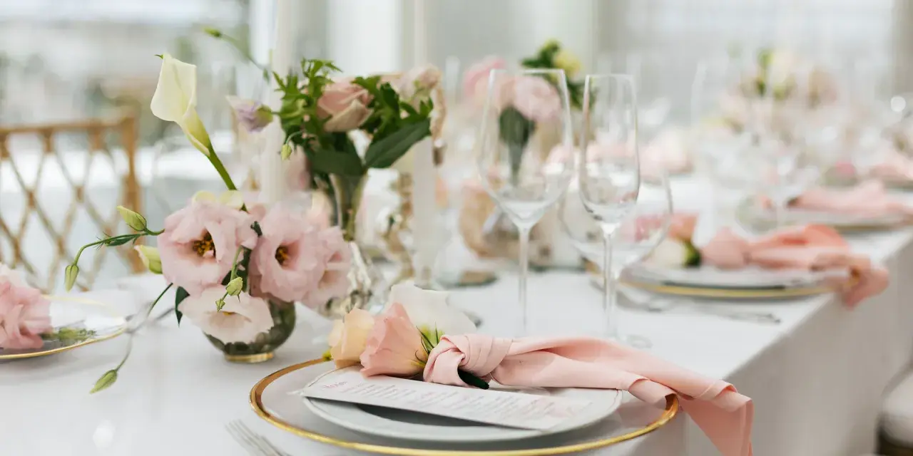 Ett vackert dukat bord med rosa dekorationer, blommor och glas. En elegant dukning för ett speciellt tillfälle.