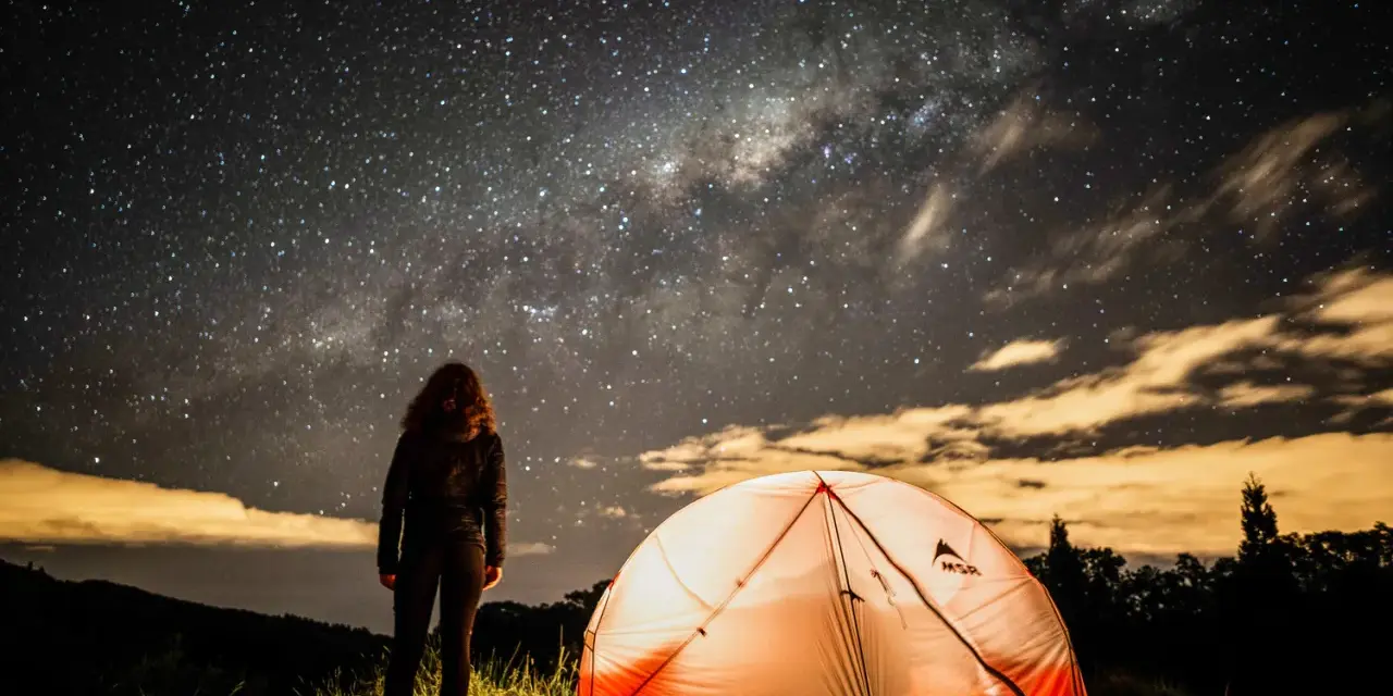 Nuit étoilée sur un bivouac GR34. Une personne admire la Voie lactée près d'une tente illuminée.