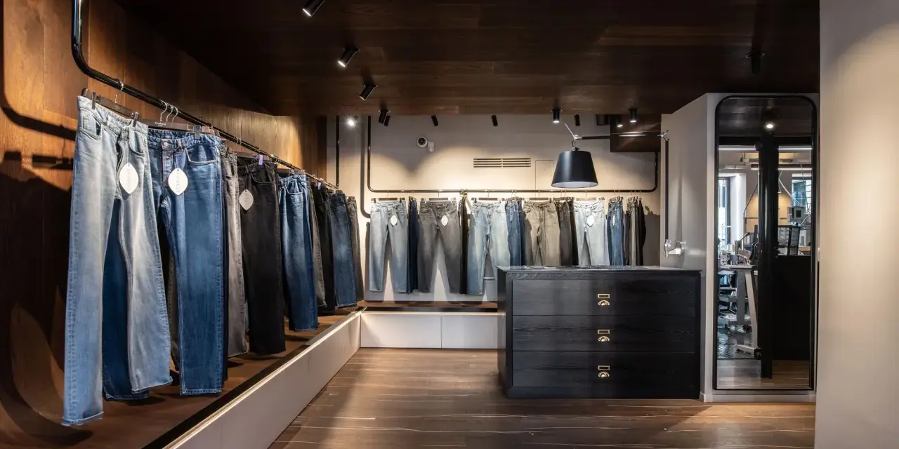 Jeans in vari lavaggi e tagli, inclusi modelli slim fit, esposti in un negozio moderno con pavimenti in legno scuro e illuminazione a faretti.