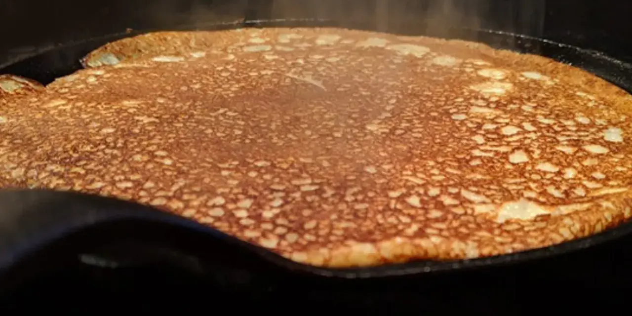 En gyllene, nygräddad pannkaka steker i en gjutjärnspanna. Perfekt för en glutenfri frukost eller fika.