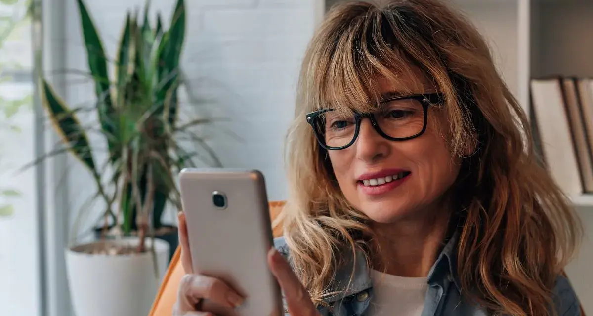 Kobieta w okularach przegląda telefon, być może szuka bratniej duszy na **Bumble w Polsce**.