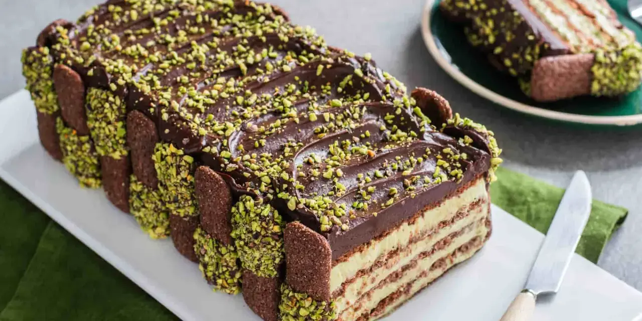 Torta fredda con strati di biscotti, crema e cioccolato, decorata con granella di pistacchio. Un tripudio di dolci al pistacchio.