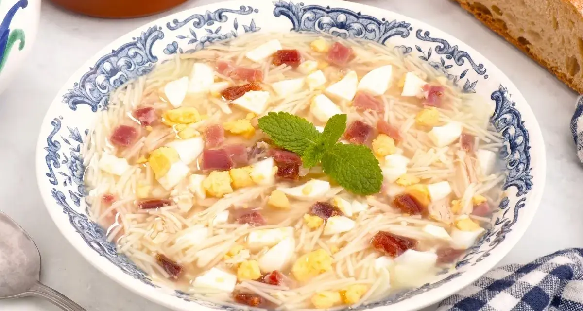 Sopa de picadillo andaluza en un plato azul y blanco con trocitos de huevo duro, jamón y fideos finos.