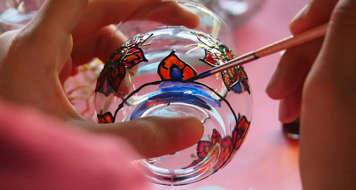 Manos pintando un vaso de cristal con flores de colores. Aprende como pintar cristal a mano y crea arte.