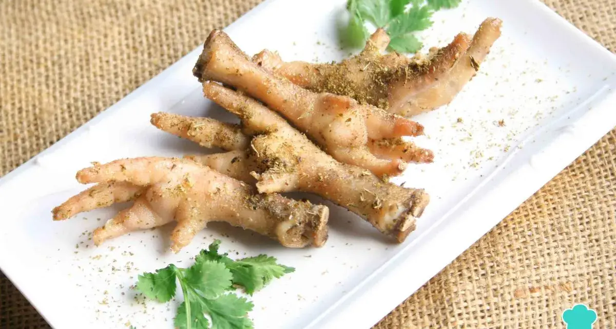 Patas de pollo sazonadas y listas para cocinar, adornadas con cilantro fresco sobre un plato blanco.