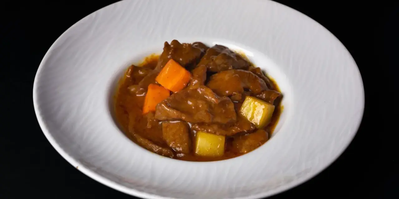 Estofado de carne con trozos de zanahoria y patata en una salsa espesa, servido en un plato blanco.