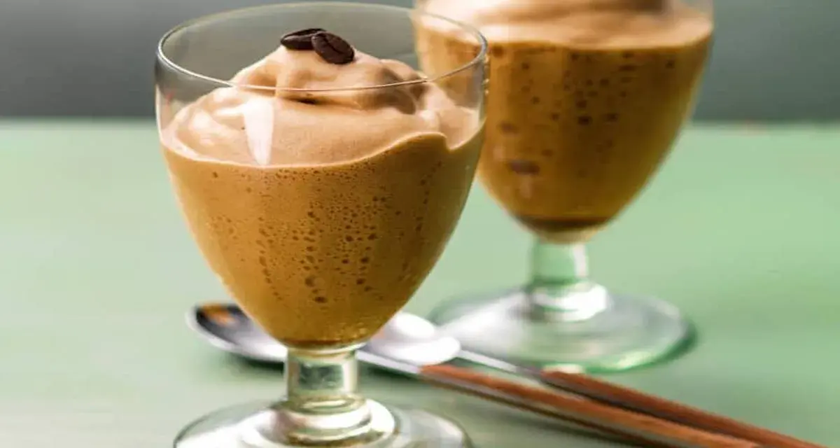 Due bicchieri di spumone al caffè, guarniti con chicchi di caffè, su un tavolo verde.
