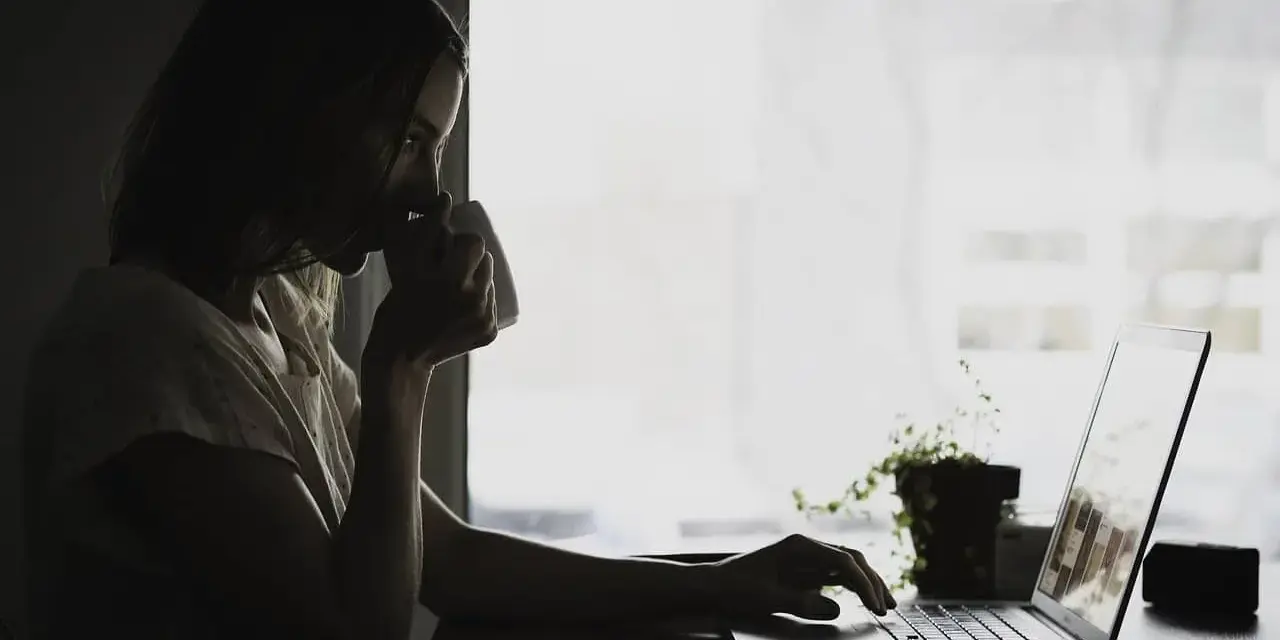 Kobieta pije kawę, pracując na laptopie. Może właśnie przegląda umowa zlecenie kierowca, planując swoją karierę.