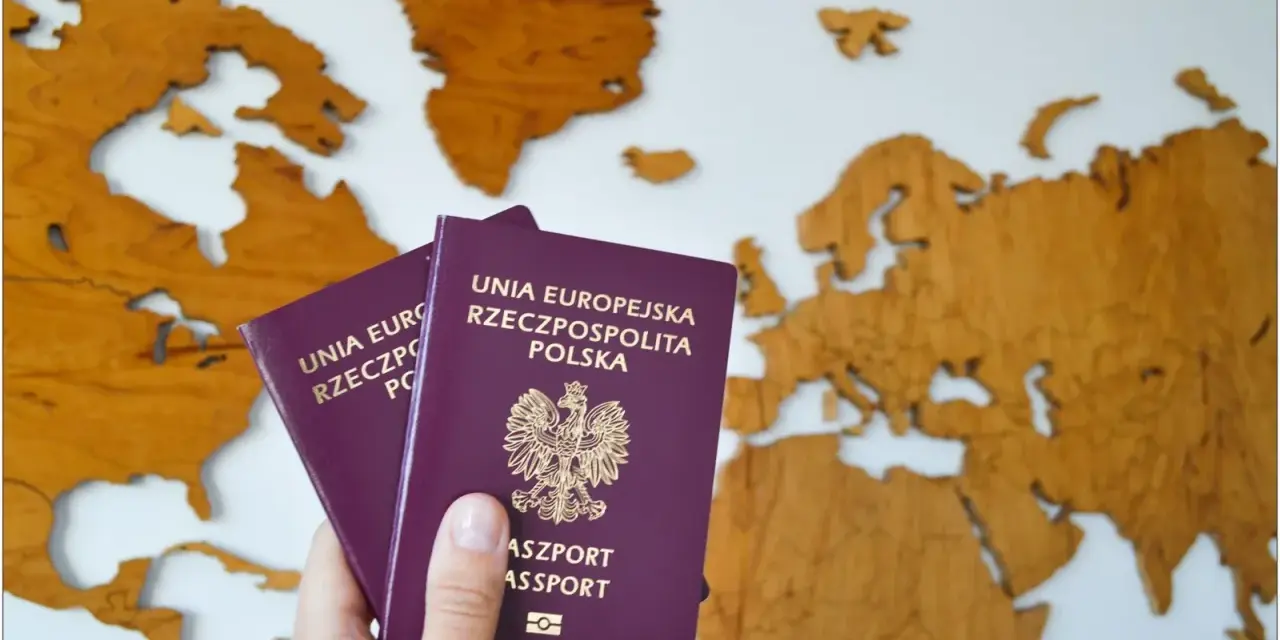 Dwa polskie paszporty w dłoni na tle drewnianej mapy świata. Planujesz podróż? Dowiedz się, jak wyrobić paszport.
