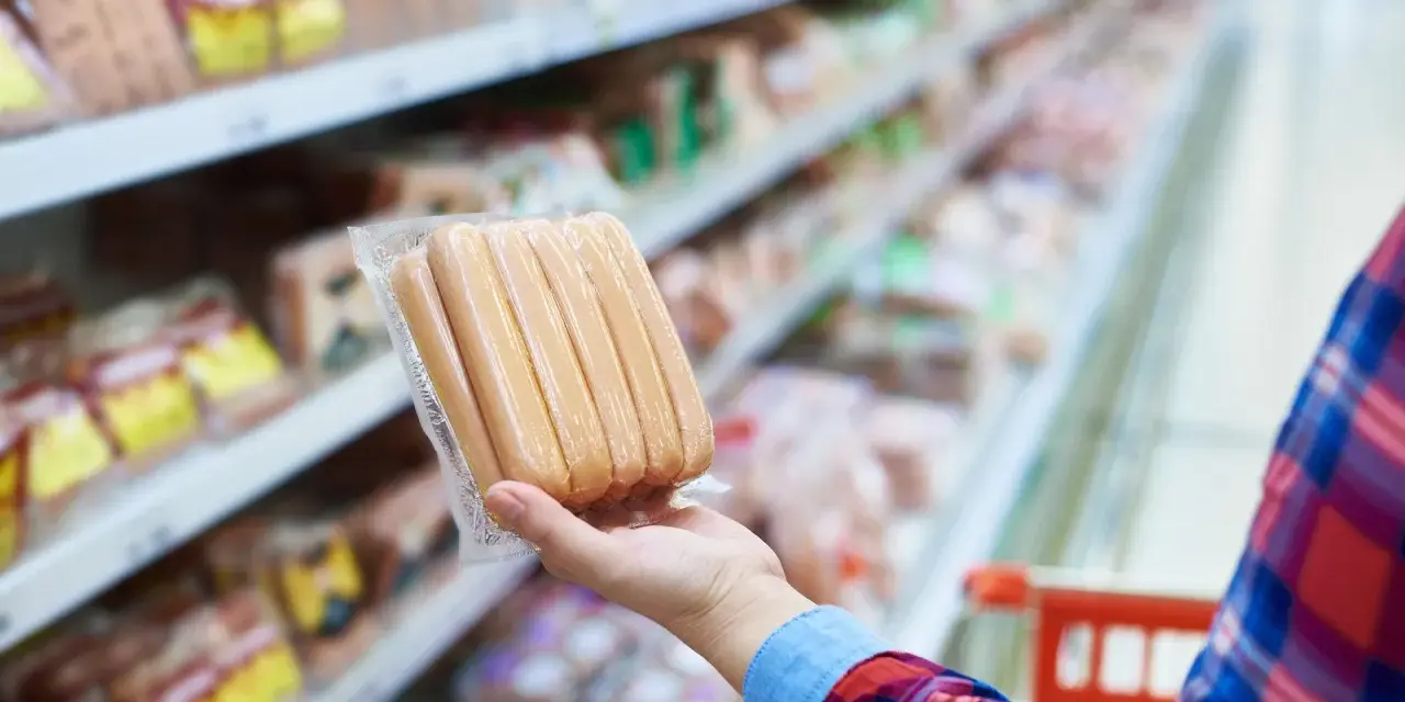 Ręka trzyma paczkę parówek w supermarkecie. Zastanawiasz się, ile kalorii ma parówka?