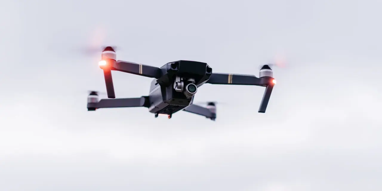 A drone hovers in the sky, its red lights blinking. Planning a trip? Be aware of Bahamas drone laws before you fly.