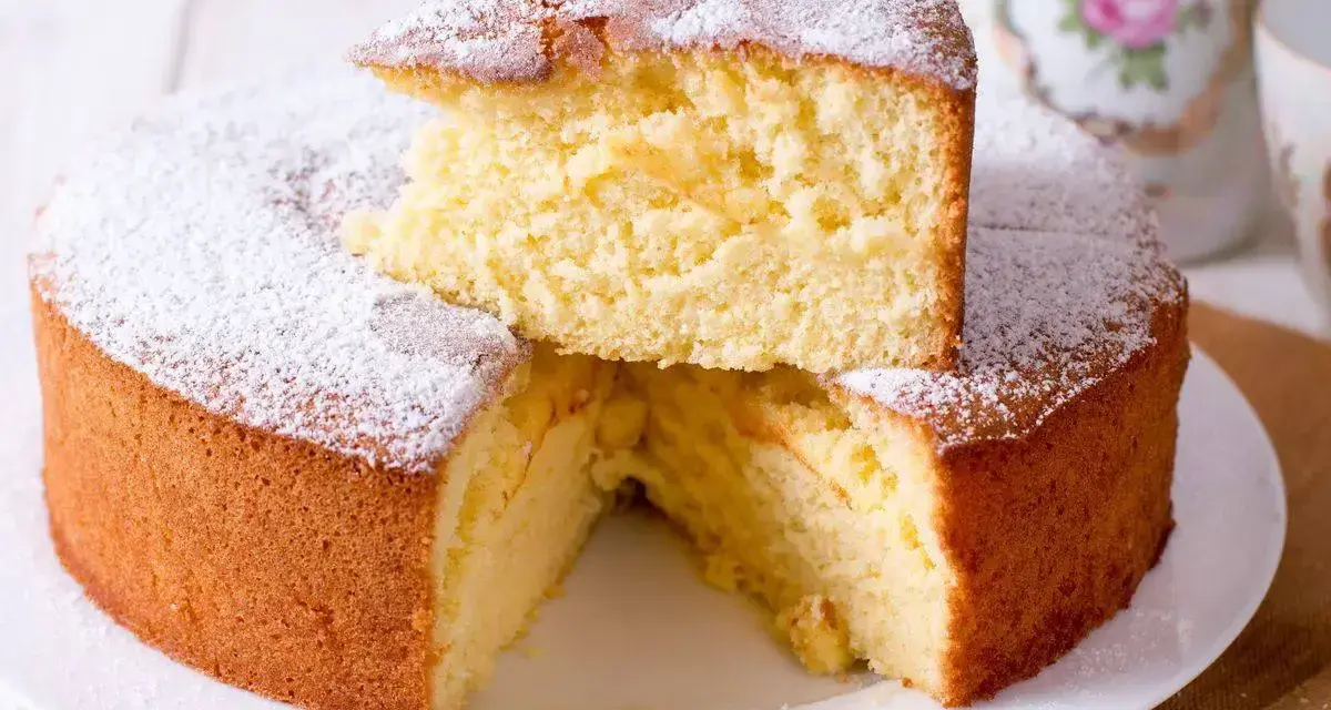 Una soffice torta fredda allo yogurt, spolverata di zucchero a velo, con una fetta sollevata che ne rivela la morbidezza.