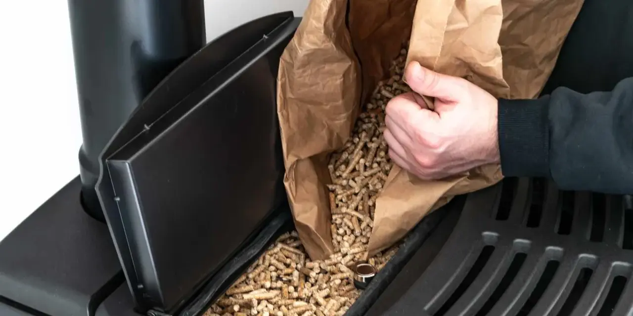 Persona rellena un compartimento de estufa de pellets. Considera el instalar estufa pellets precio para un hogar eficiente.