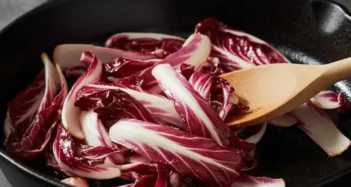 Fette di radicchio rosso vengono saltate in padella con un cucchiaio di legno.