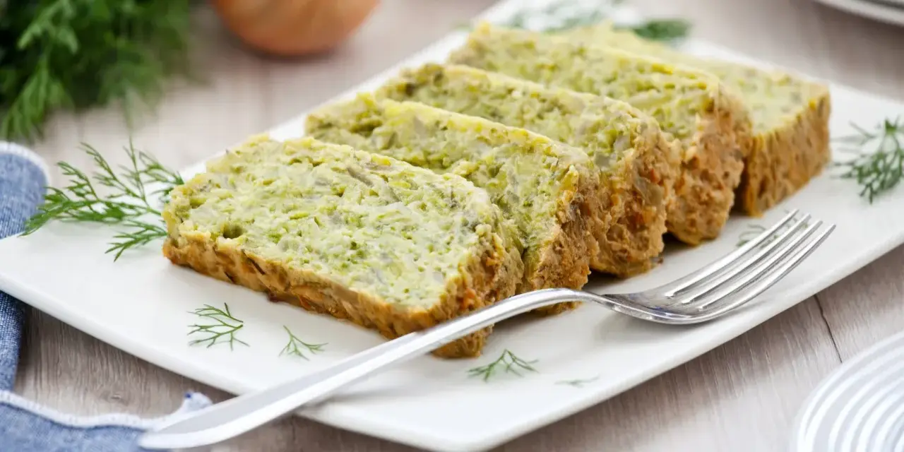 Fette di flan di zucchine su un piatto bianco, guarnite con aneto. Una forchetta argentata è appoggiata sul piatto.