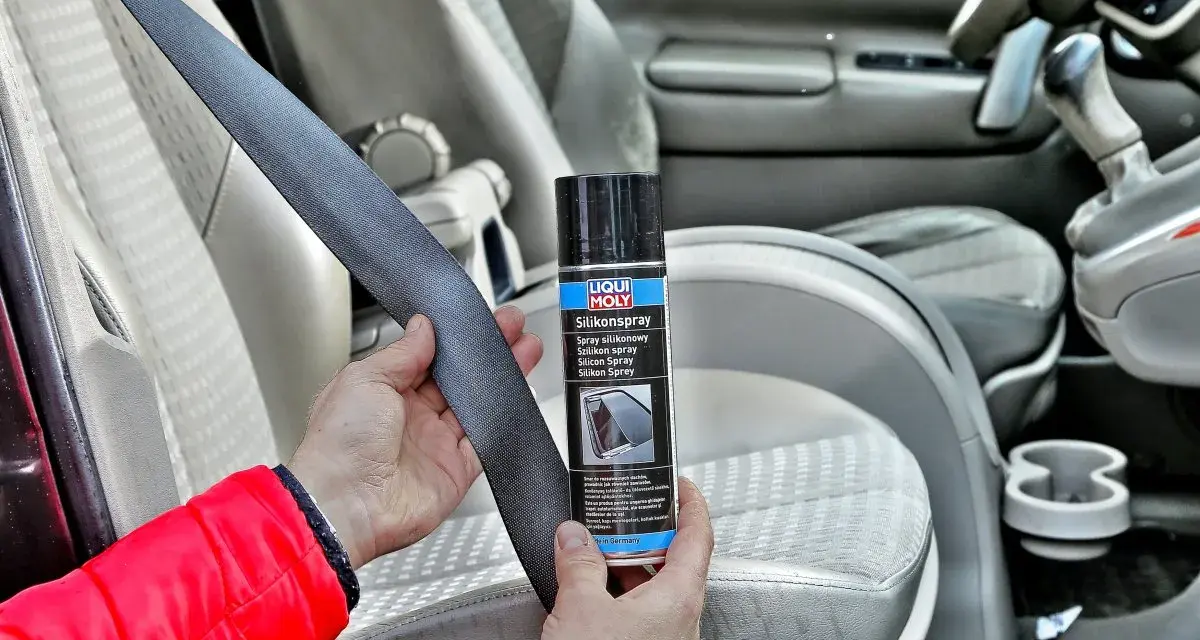 Ręce trzymają pas bezpieczeństwa i puszkę z napisem "Silikonspray". Dowiedz się, jak usunąć silikon z materiału w samochodzie.