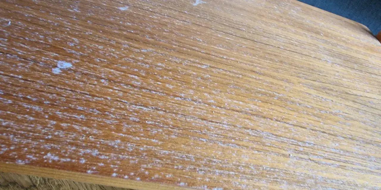 Detaljerad bild av en sliten teakskiva, redo för att renovera teakbord. Vita fläckar och repor syns tydligt.