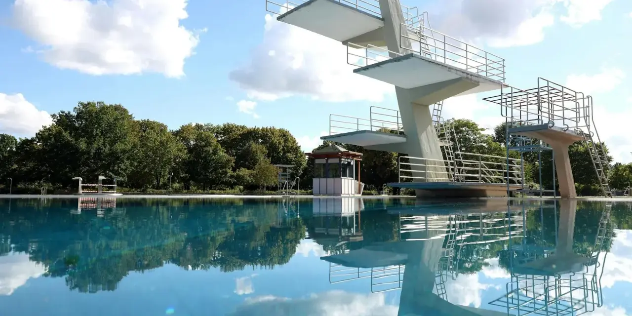Sprungturm im Schwimmbad Pankow spiegelt sich im klaren Wasser. Ein sonniger Tag lädt zum Sprung ein.