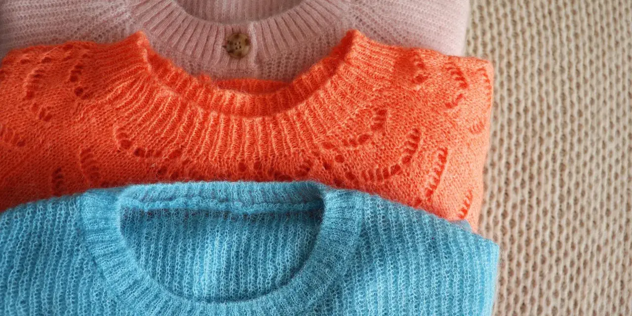 Gestapelte Pullover in Rosa, Orange und Blau. Zeit für die **Wolle waschen**, damit sie wieder flauschig sind.