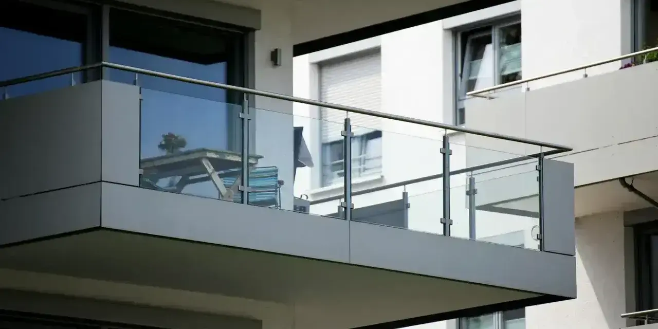 Nowoczesna loggia z przeszkloną balustradą, na której stoi stolik z kwiatami i krzesło.