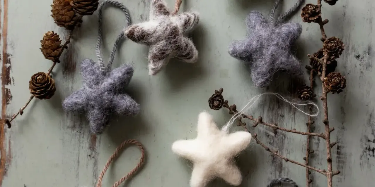 Mjuka, filtade julstjärnor i grått och vitt, som påminner om klassiska julpyssel. Dekorerade med kottar och grenar på en sliten träbakgrund.
