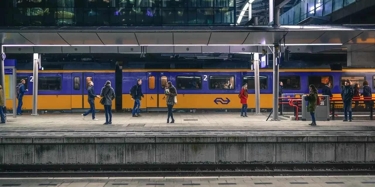 Ludzie na peronie czekają na niebiesko-żółty pociąg na nowoczesnej stacji kolejowej.