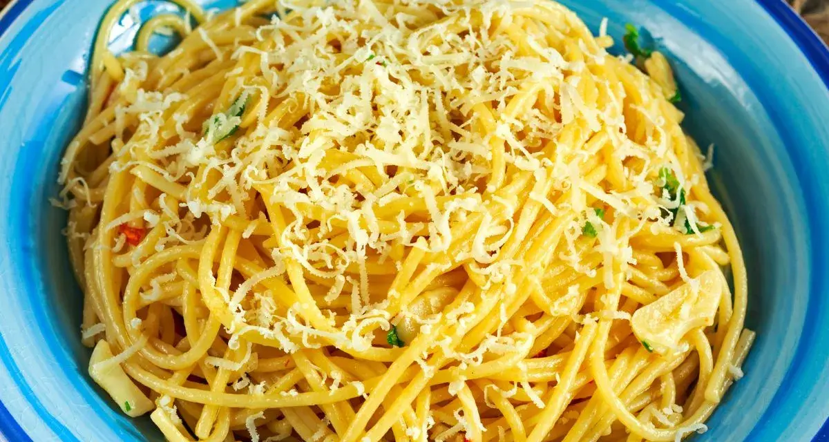 Porcja spaghetti z tartym serem i ziołami w niebieskiej misce.