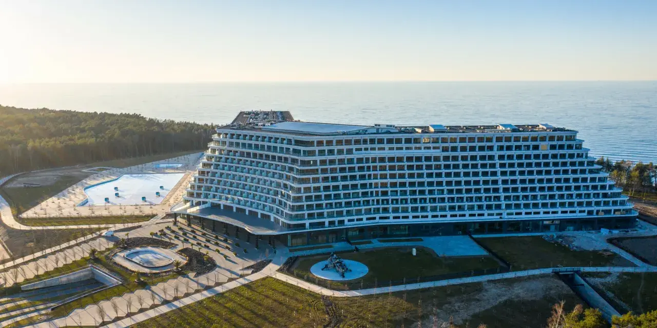 Nowoczesny, falisty pobierowo nowy hotel z basenami i widokiem na morze, otoczony lasem.