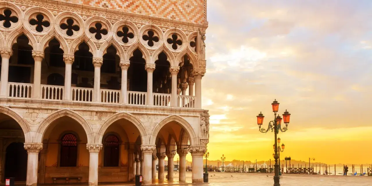 Palazzi storici di Venezia all'alba, con il sole che illumina la piazza e le architetture gotiche.