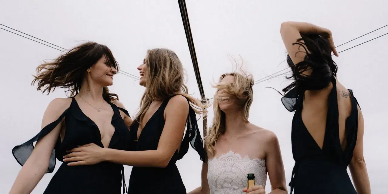 Sorelle della sposa, con abiti neri eleganti, celebrano il matrimonio con champagne. Accessori per abito nero matrimonio perfetti per un look sofisticato.