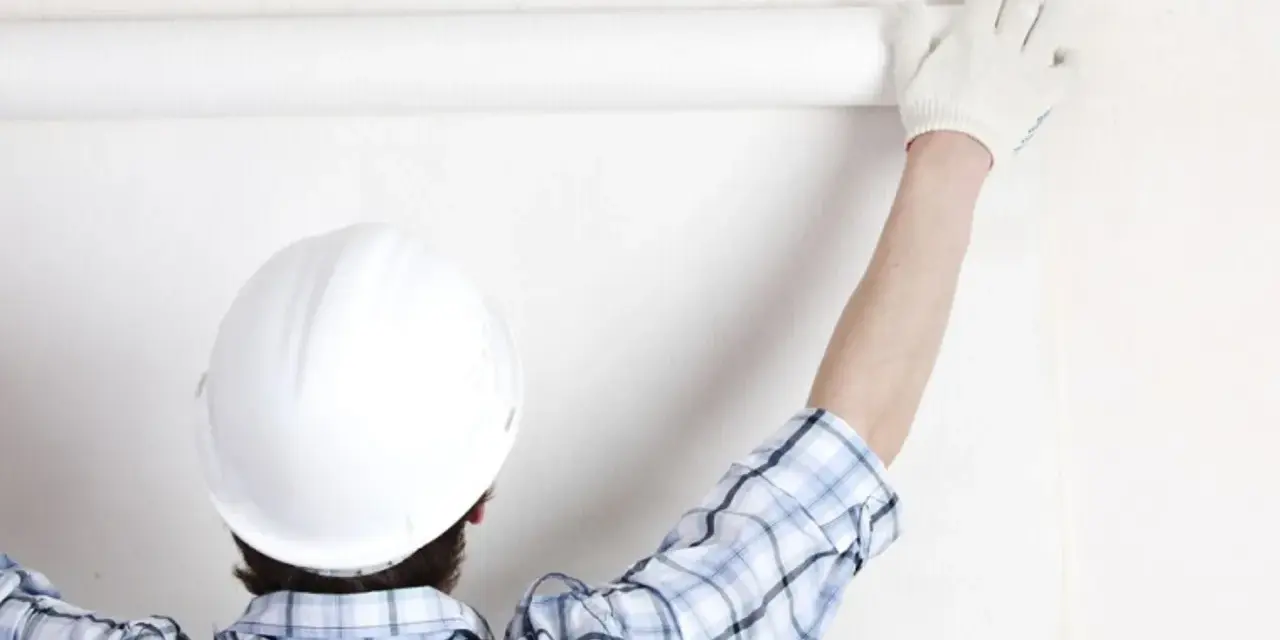Un ouvrier en casque blanc déroule une **pose toile de verre** sur un mur blanc.