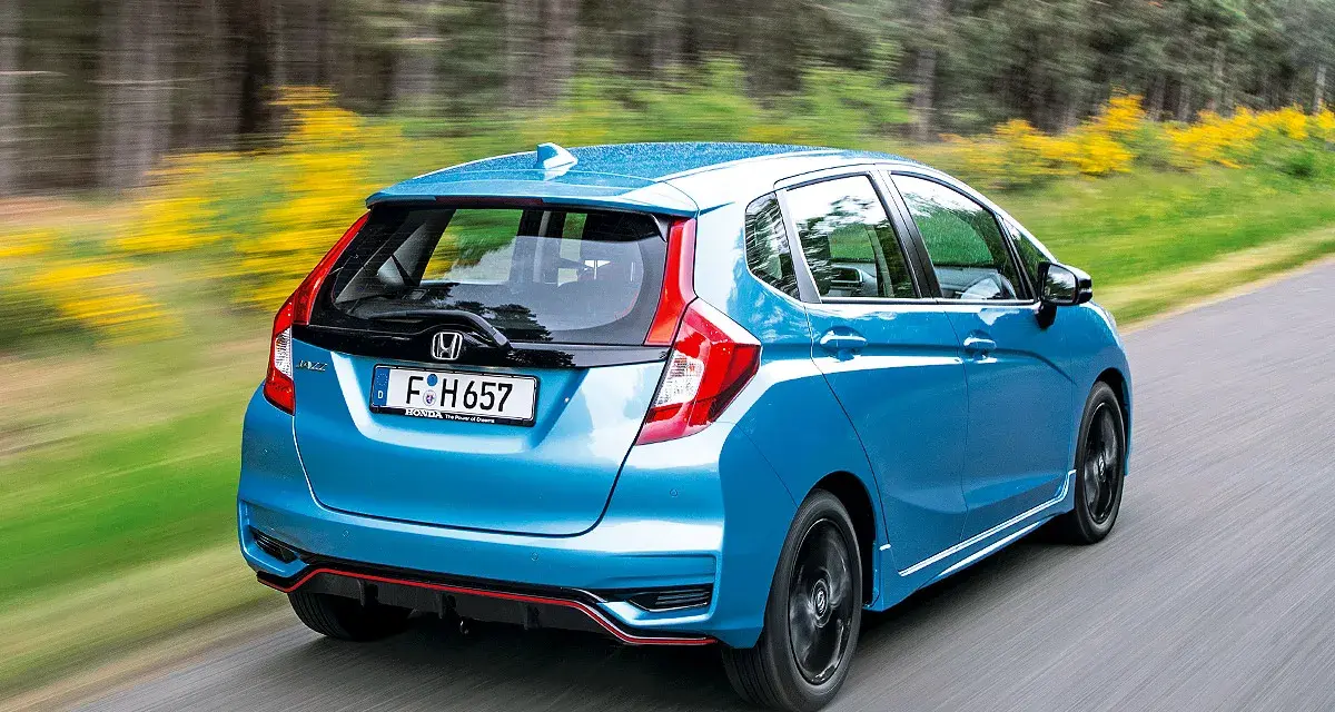 Blauer Honda Jazz Hybrid fährt auf einer Landstraße. Trotz der schönen Fahrt gibt es Berichte über Honda Jazz Hybrid Probleme.